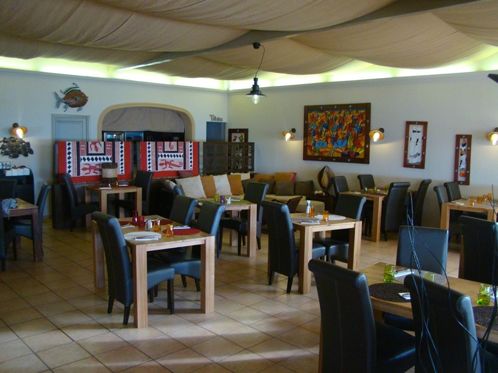 Le coin décor de la salle : tableau coloré, poisson peint, banquette et tables dressées