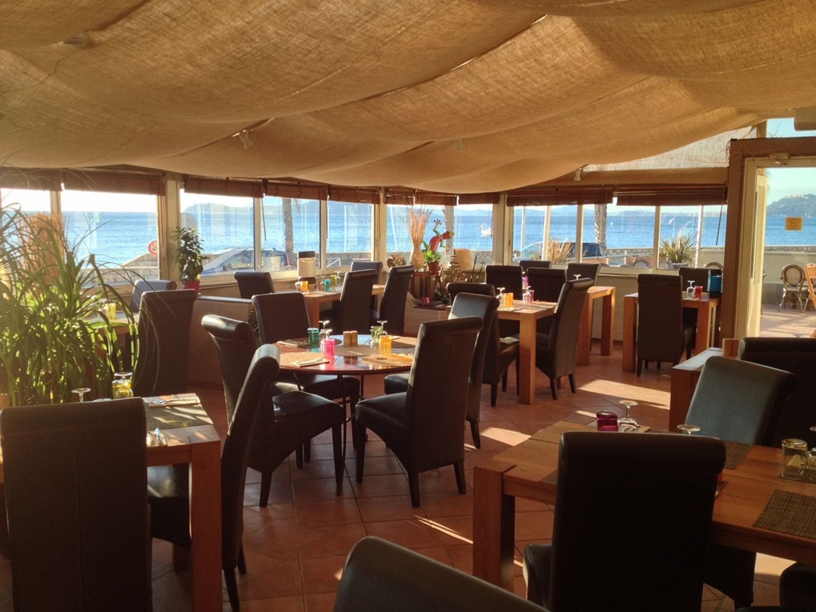La salle de jour : tables en bois, fauteuils en cuir, grandes baies vitrées ouvertes sur la mer