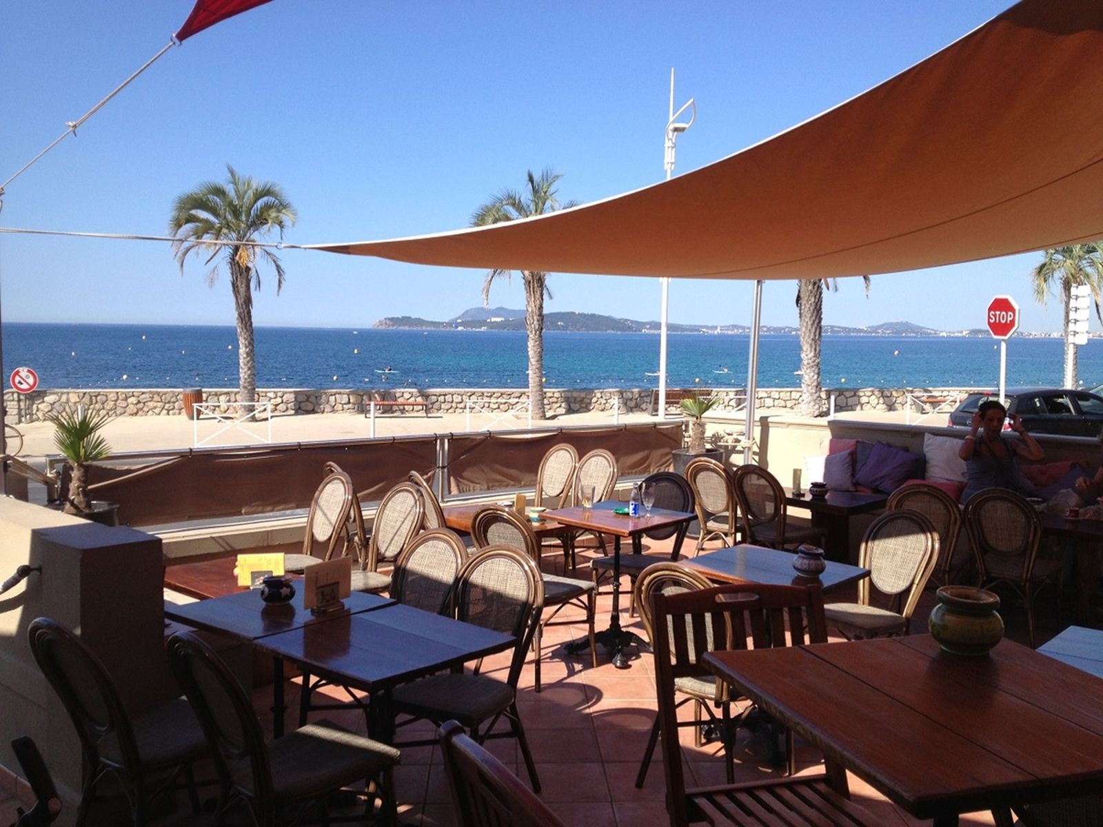 La terrasse sous ses voiles, tables en bois et chaises, palmiers et mer bleue en arrière-plan